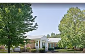 Front view of Milford Center building with white facade, columns, and surrounding trees.