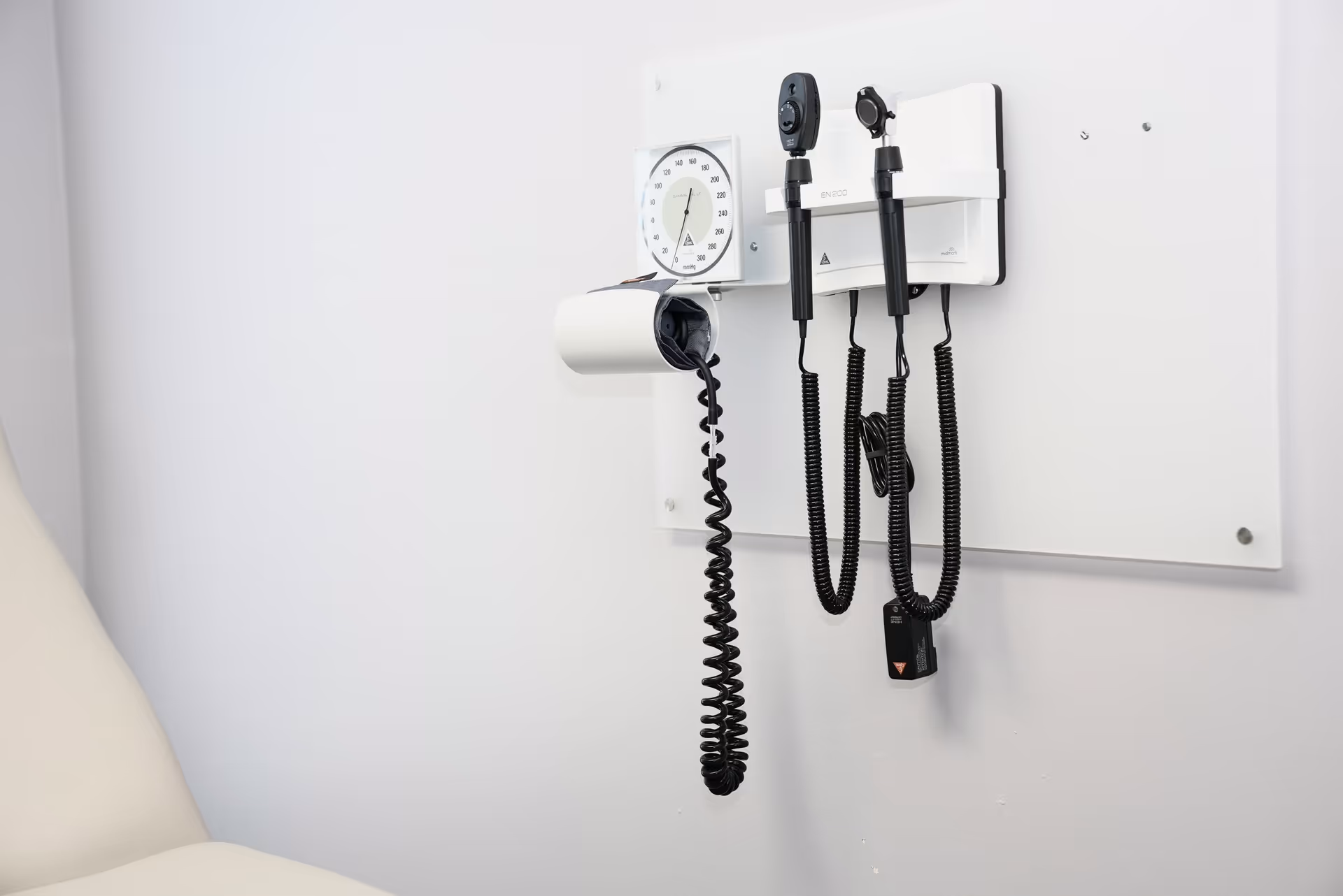 Wall-mounted medical equipment including a blood pressure cuff and stethoscope in a clinic exam room.