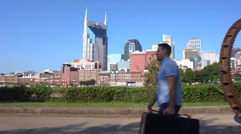 A man walks with a briefcase along a sidewalk with a city skyline behind.