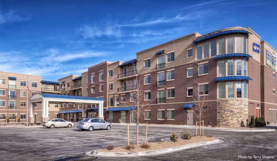 Exterior view of HighPointe Assisted Living and Memory Care building with brick facade and blue awnings.
