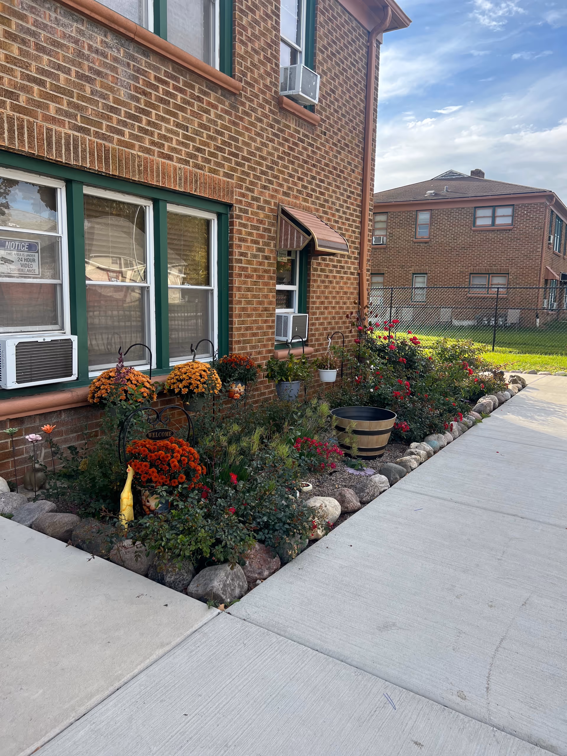 Brick apartment building exterior with a colorful flower garden along the walkway.