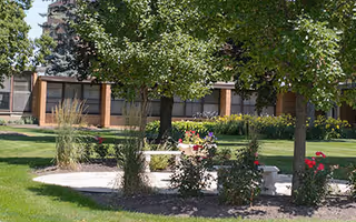 Exterior view of Bridgeway Senior Living building, with trees, lawn, and flower planters.