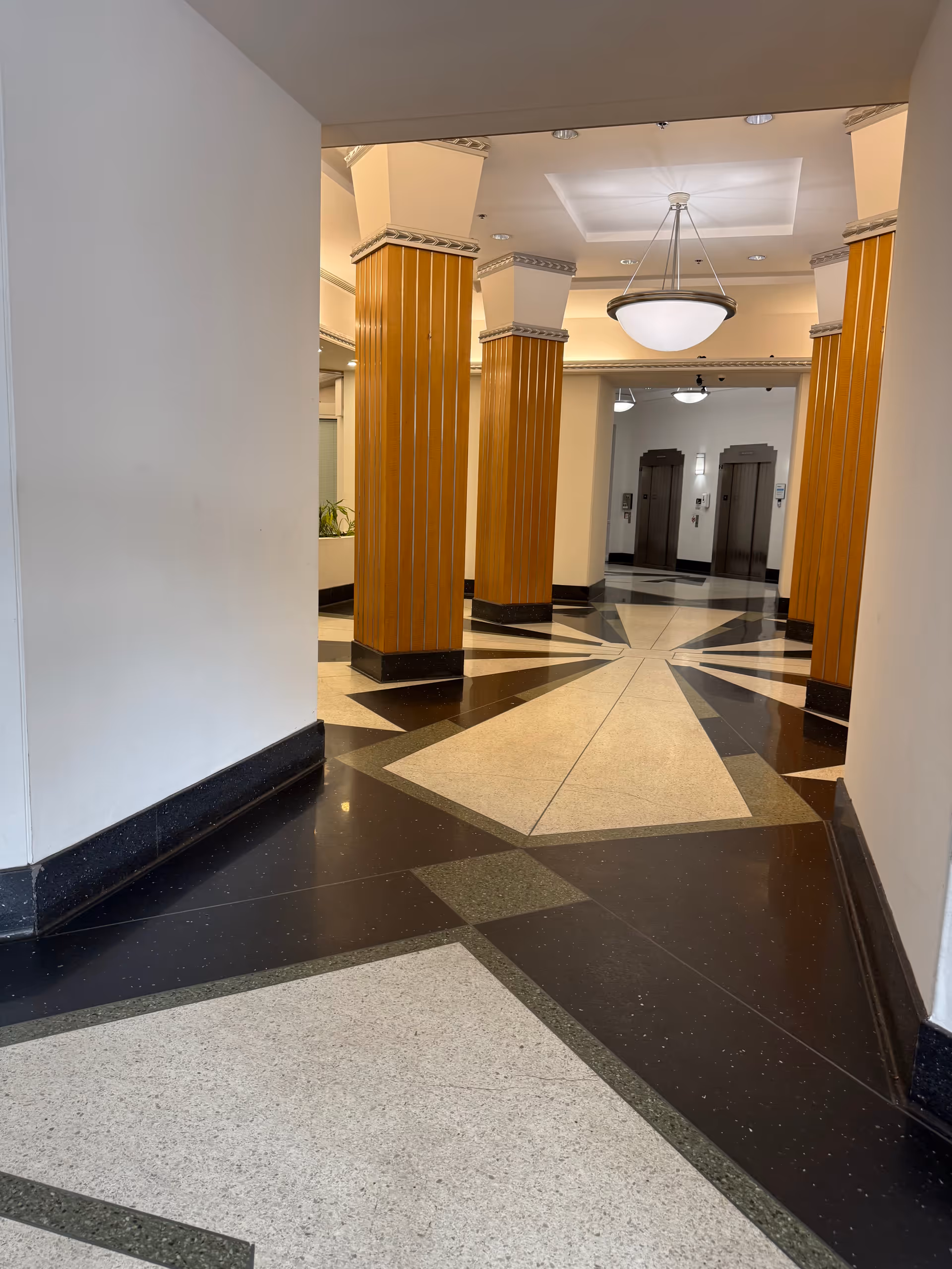 A spacious indoor corridor with decorative columns, tiled floor patterns, and elevators in the distance.