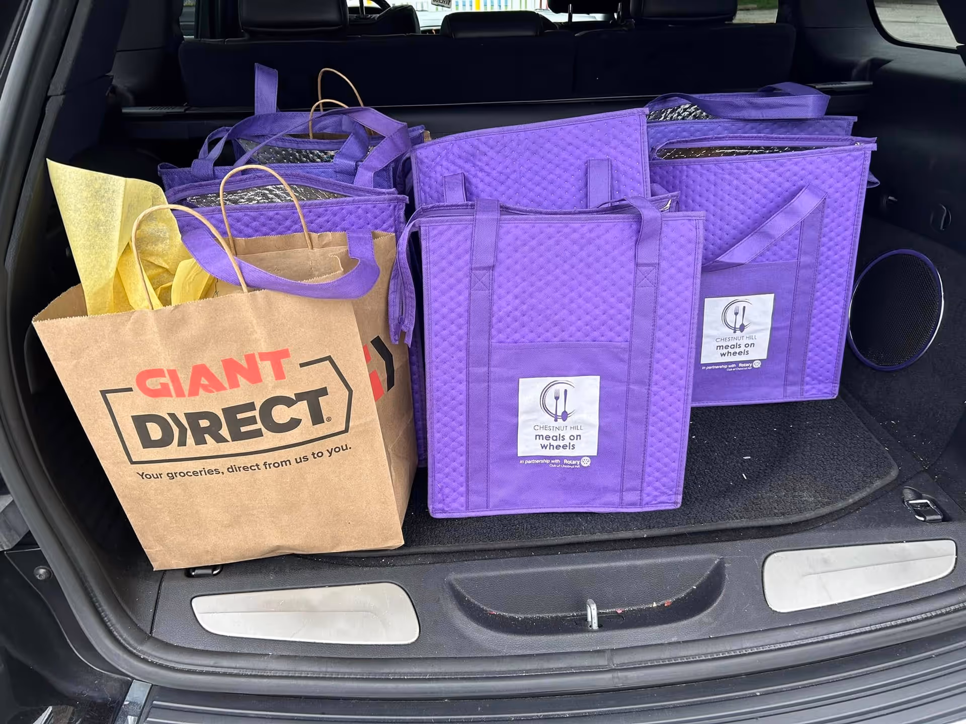 Open car trunk filled with grocery and purple meal-delivery bags.