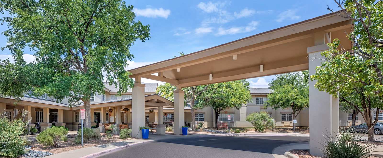 Exterior view of Brookdale Midland entrance with a covered drop-off and trees.