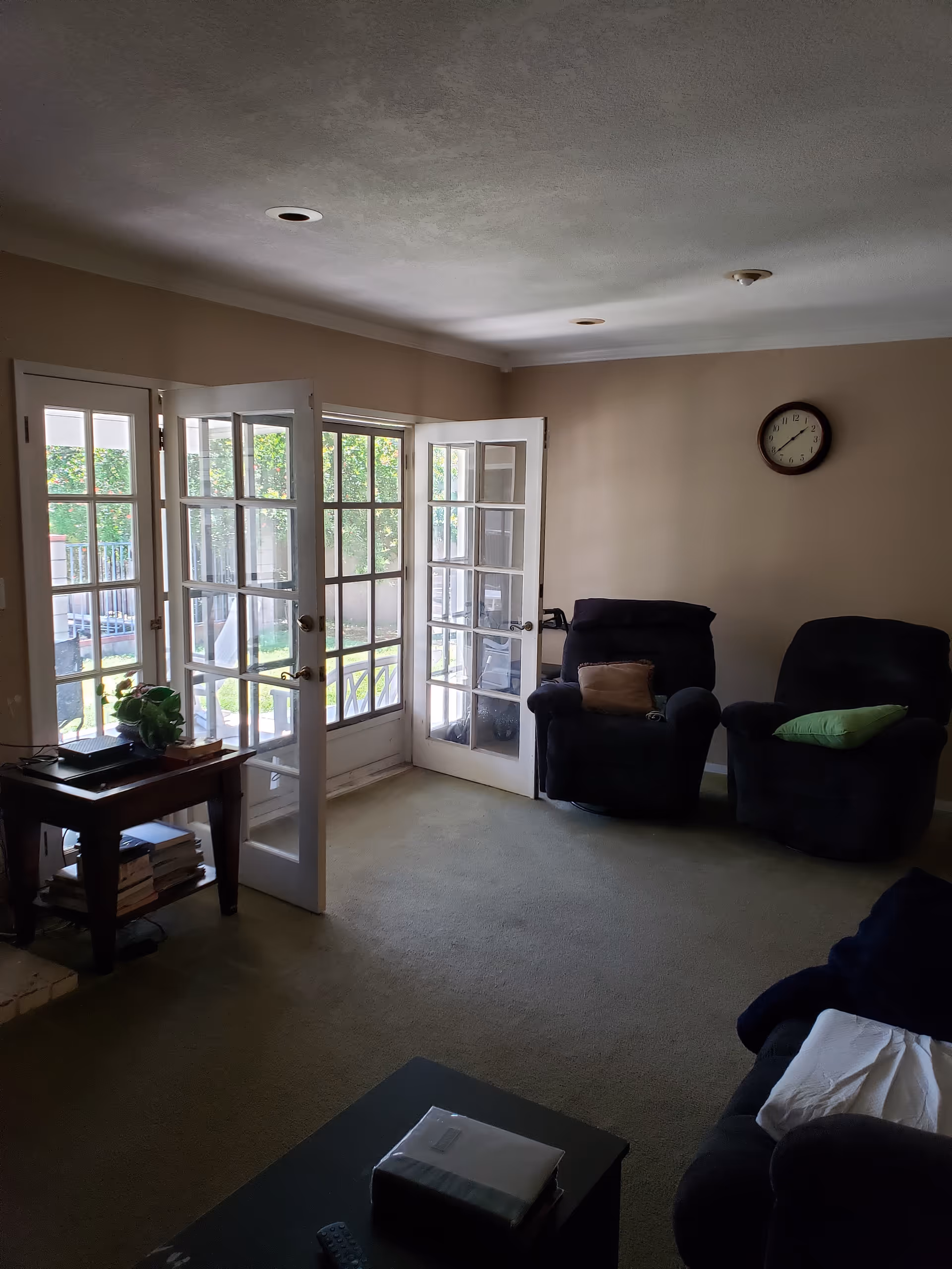Living room with French doors opening to outside, two recliners, clock, and a side table.