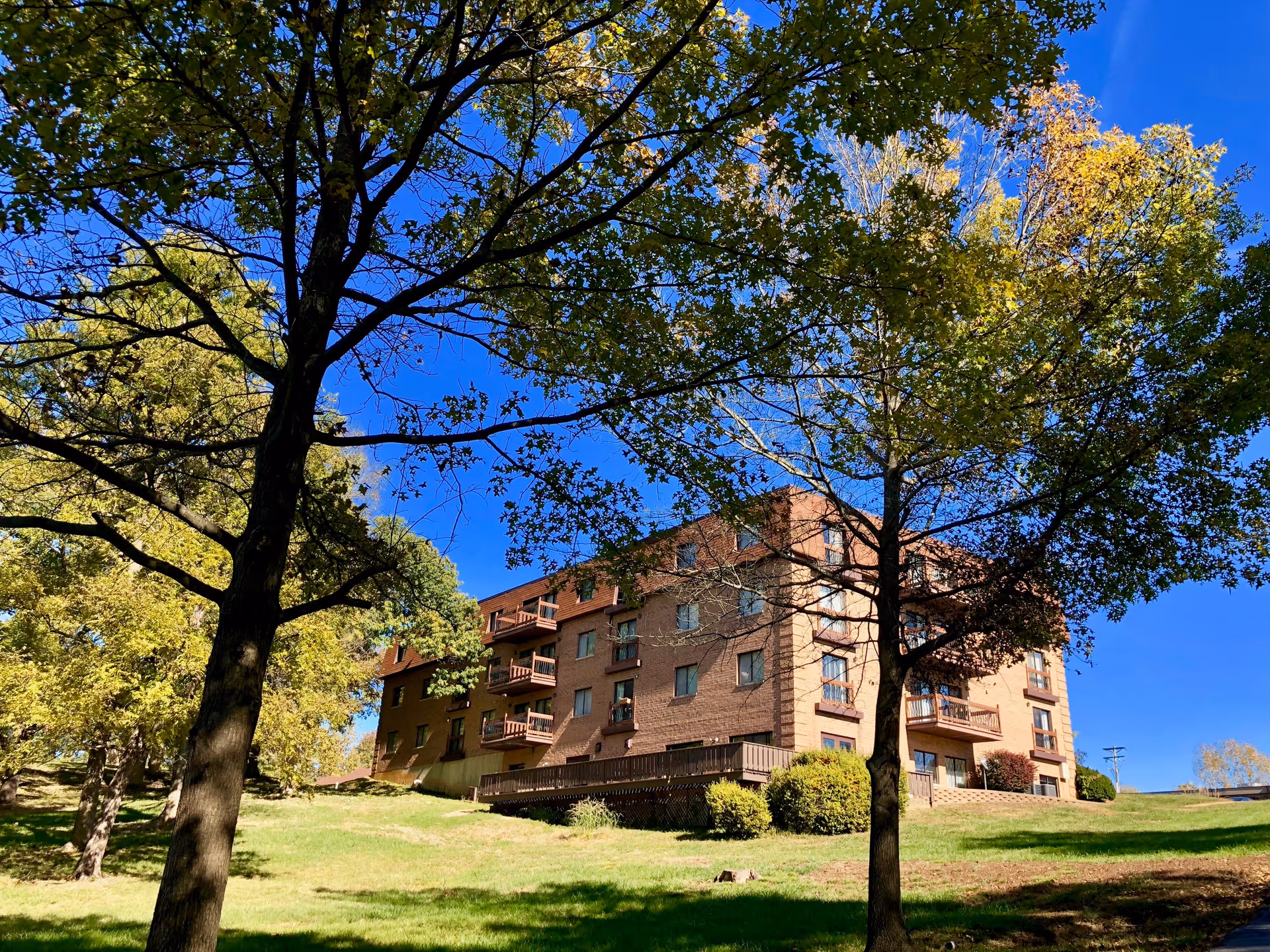 Marymount Manor residential building on a grassy hill beneath leafy trees and blue sky.