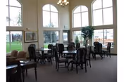 Bright dining area with large arched windows, round tables, and many chairs.