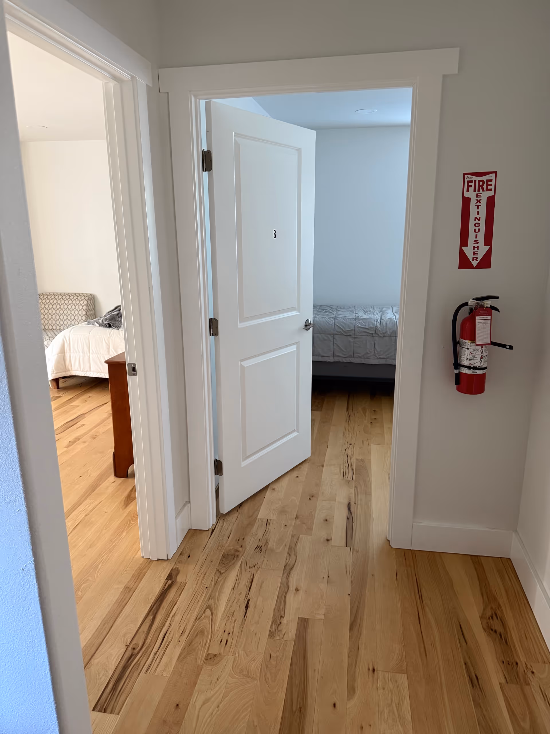Bright hallway with open bedroom doors, wooden floors, and a fire extinguisher on the wall.