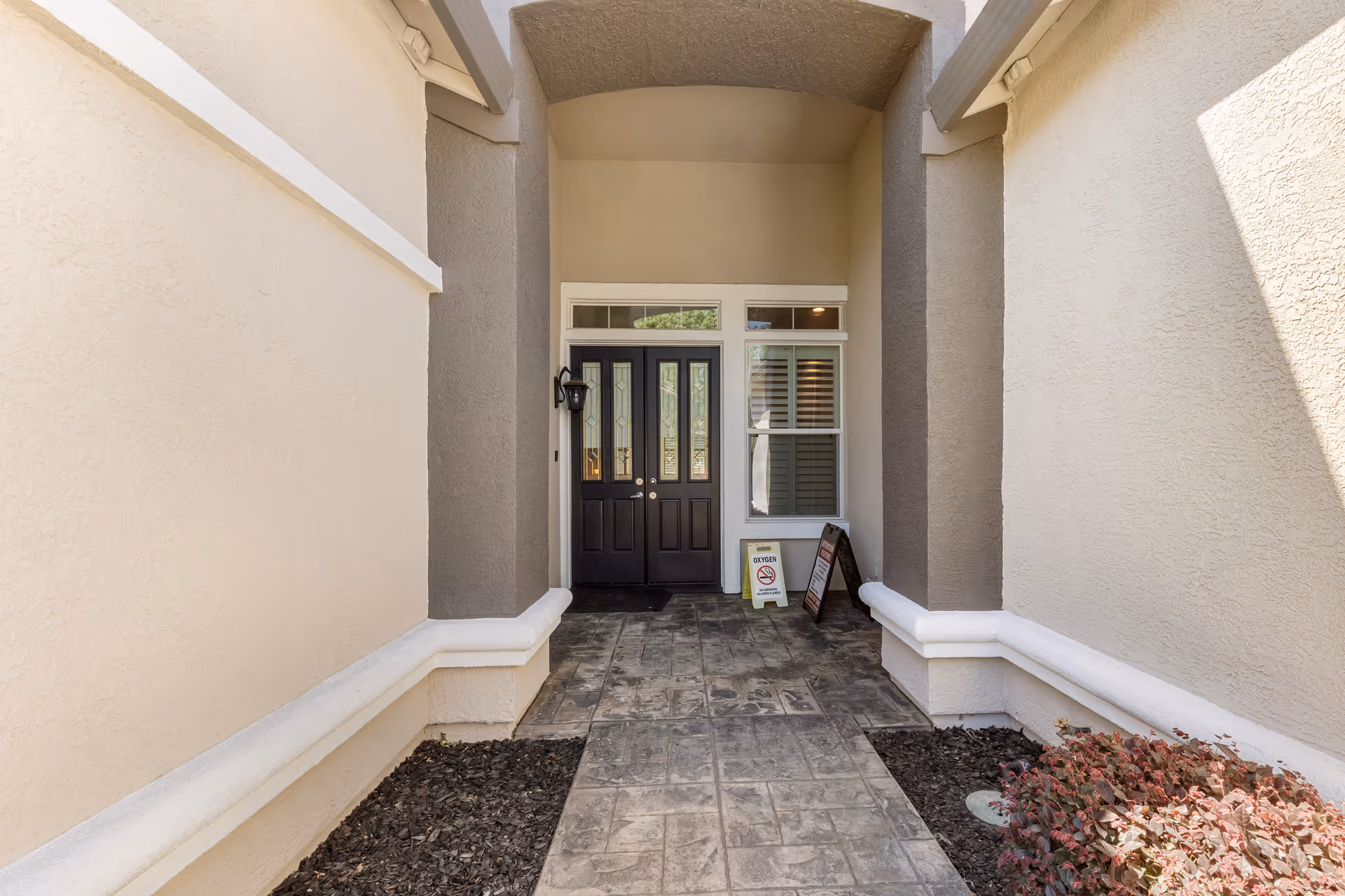 Symmetrical entryway with double dark doors, tan walls, and a stone-tiled walkway.