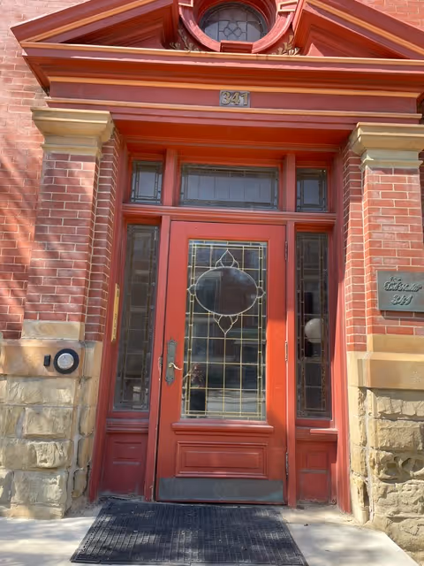 Red front door with decorative glass, brick facade, and stone base at building entrance.