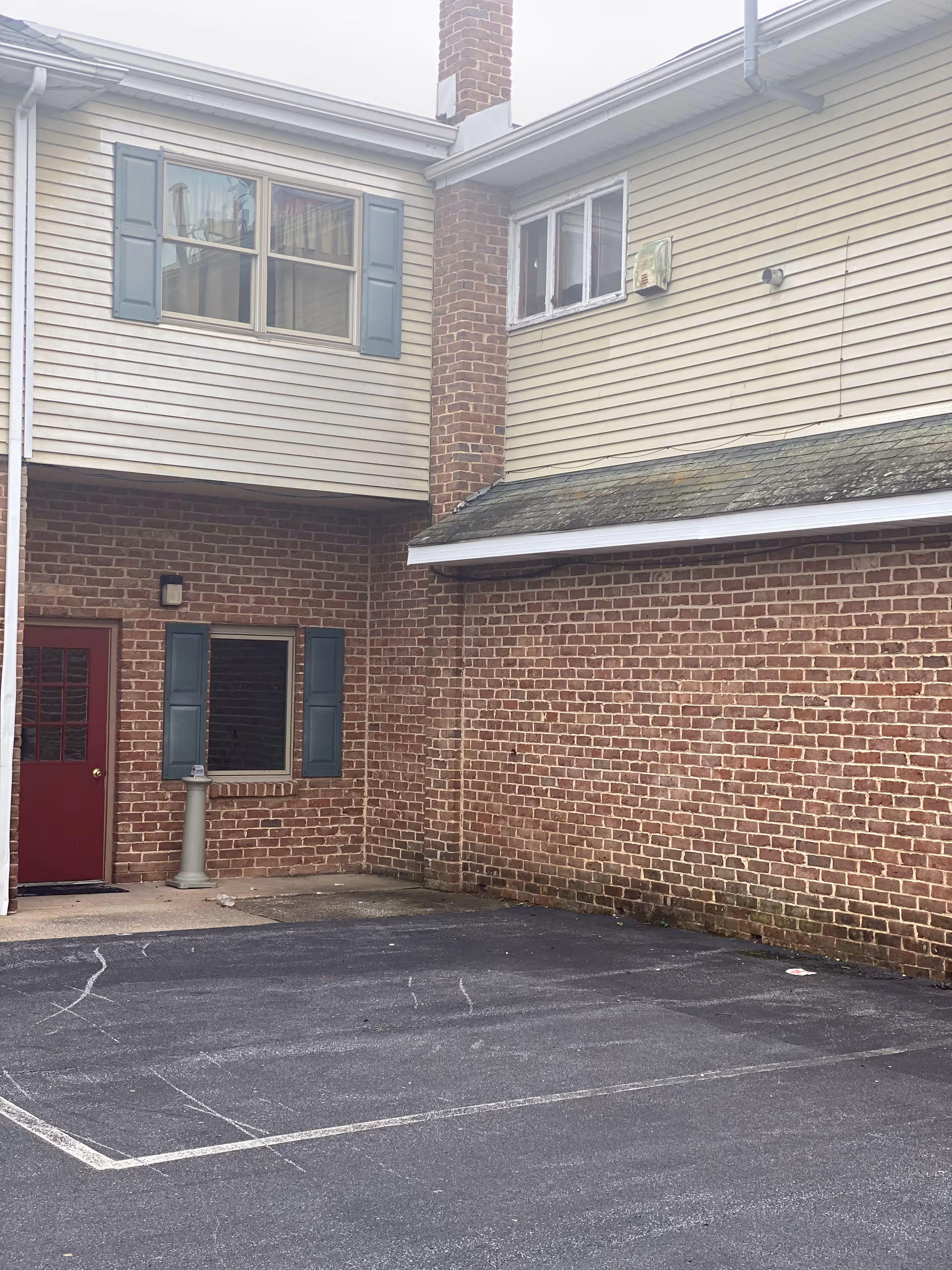 Brick exterior of a senior living facility with a red door, shutters, and parking.