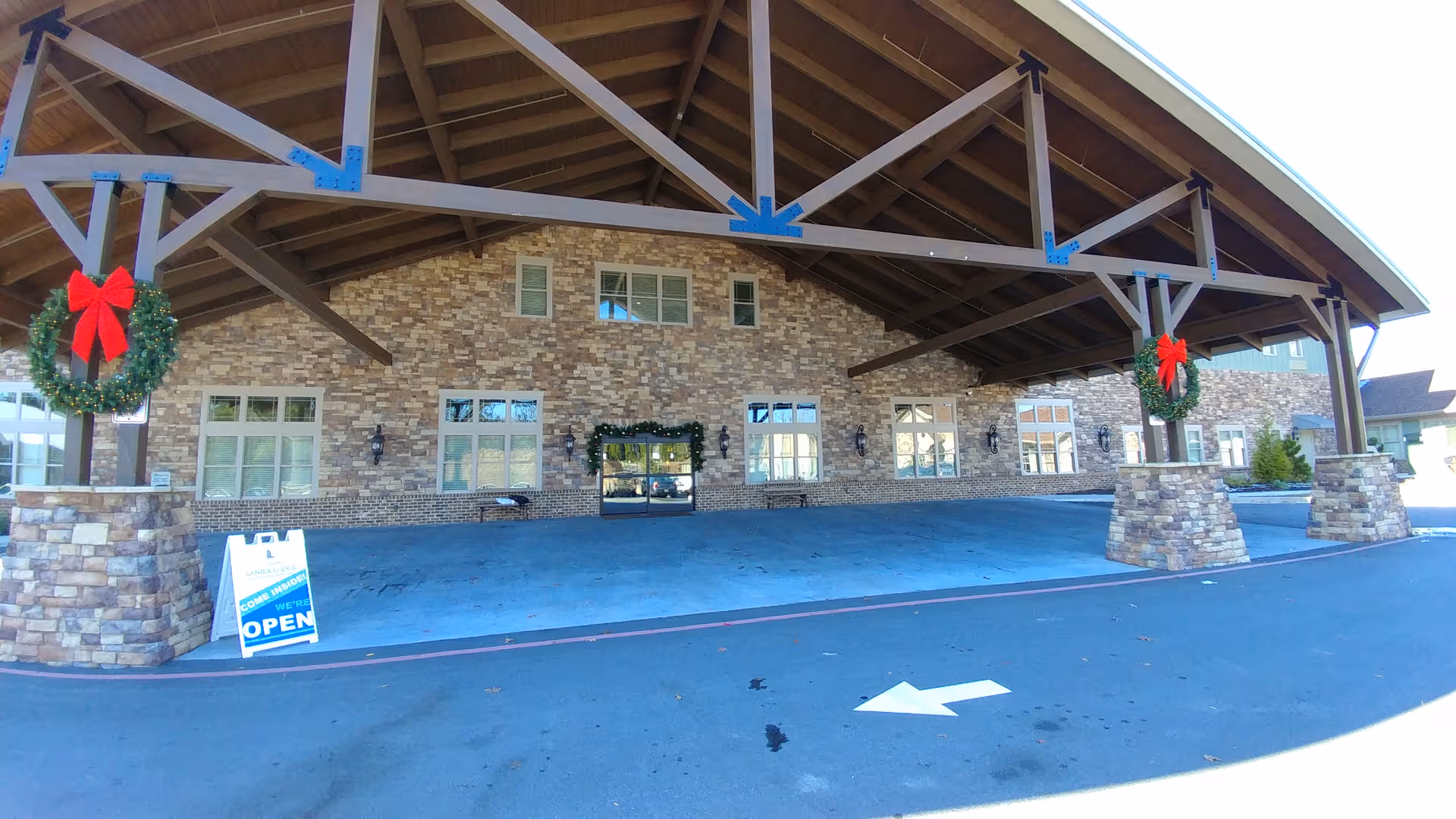Front entrance of a brick senior living facility under a large wooden porte-cochère with wreaths.