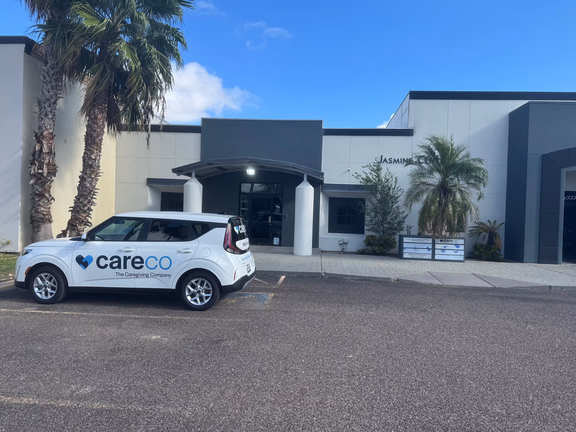 Exterior view of CareCo facility with a branded white car parked in front near palm trees.