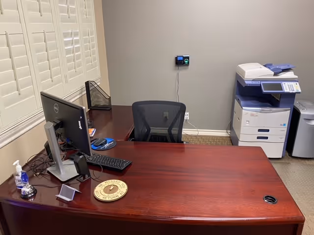 A wooden desk with computer, chair, and a copier in a small office.