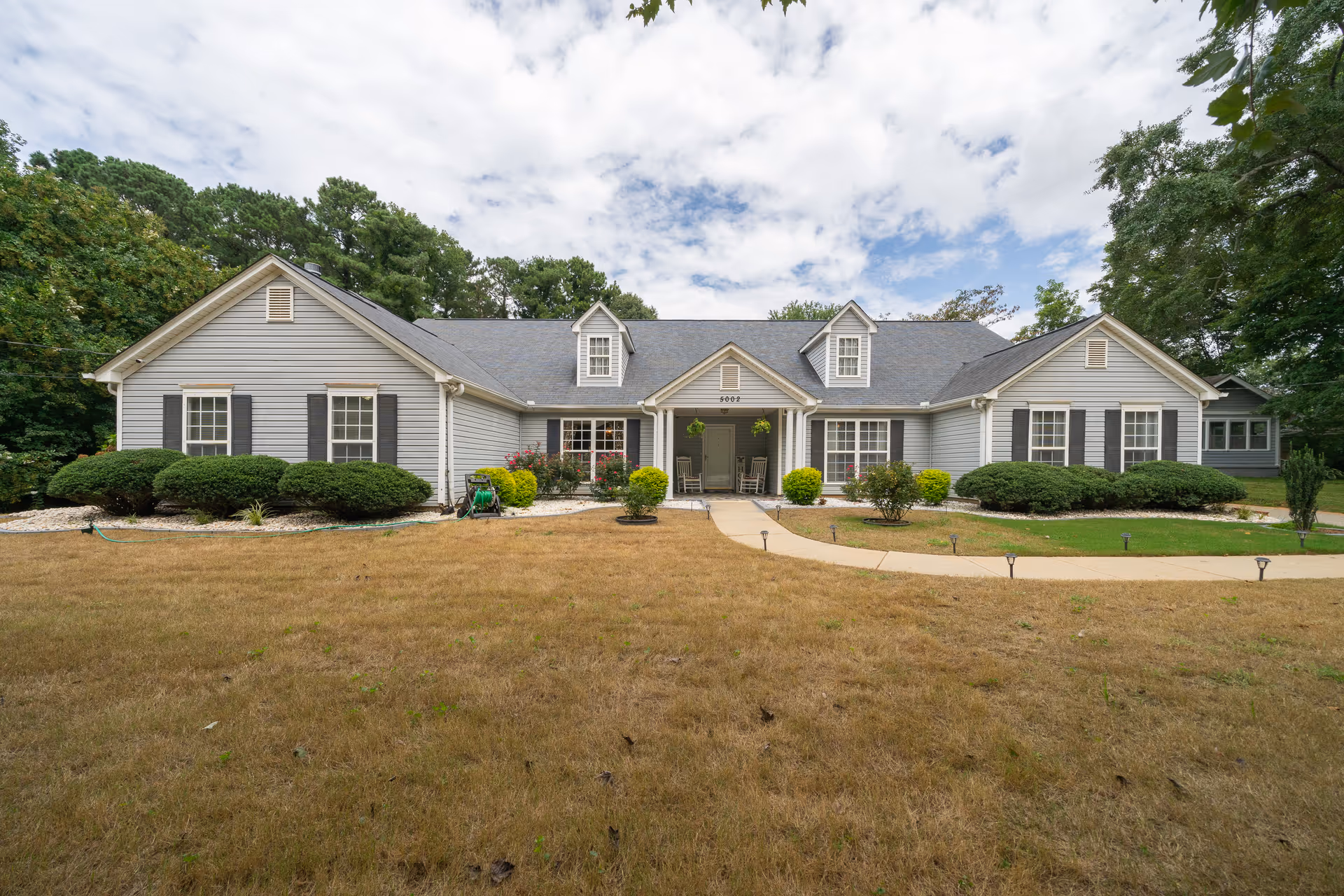 A single-story gray building with dormers, a curved path, and landscaped front yard.