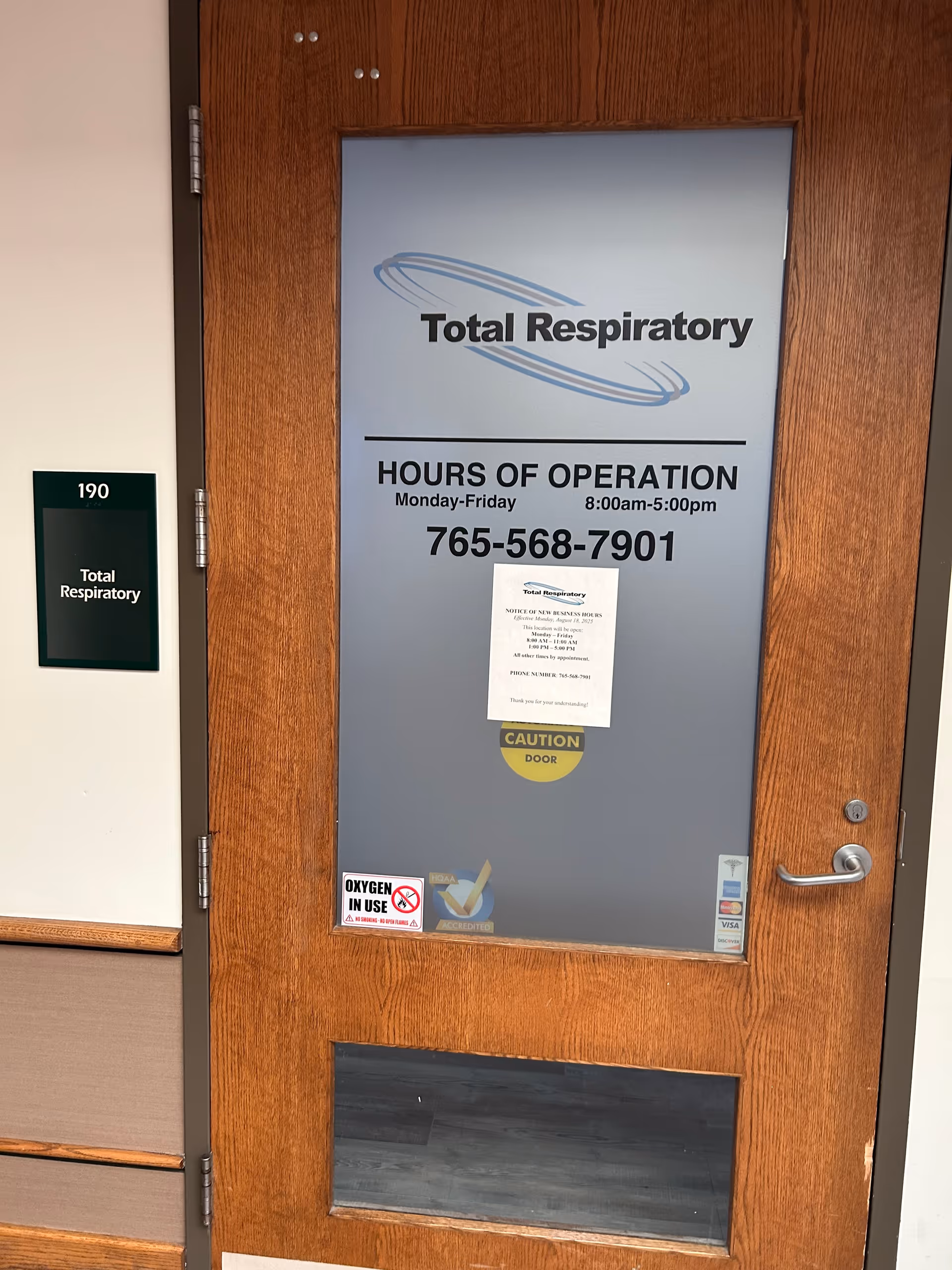 Wooden door with Total Respiratory sign and hours posted in a facility corridor.