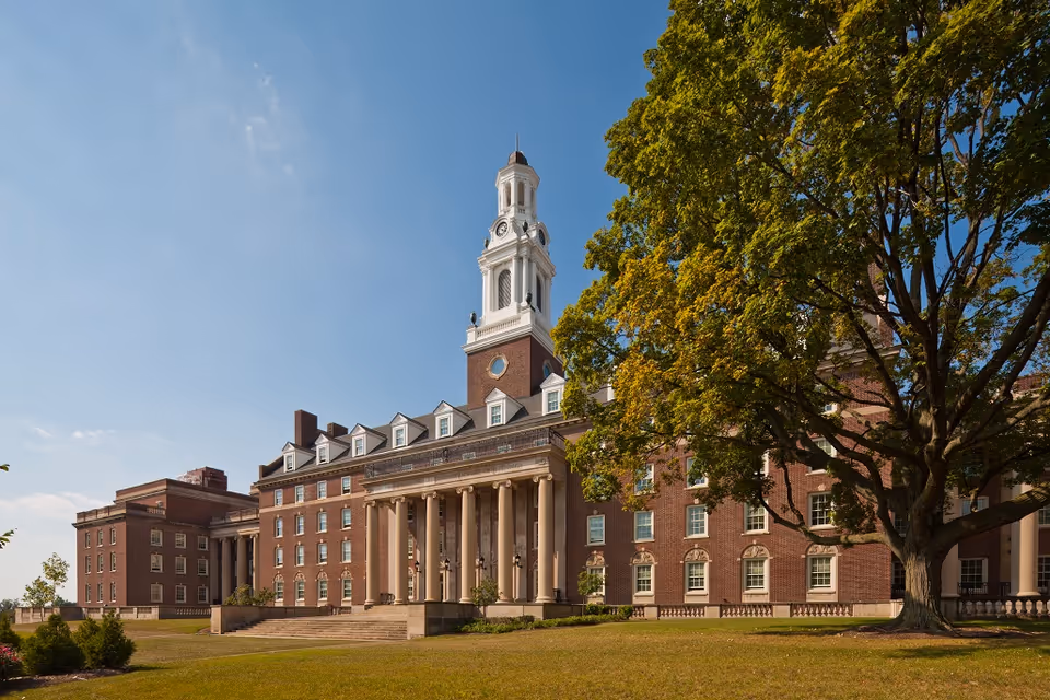 Brick building with columned entrance, clock tower, and surrounding lawn.