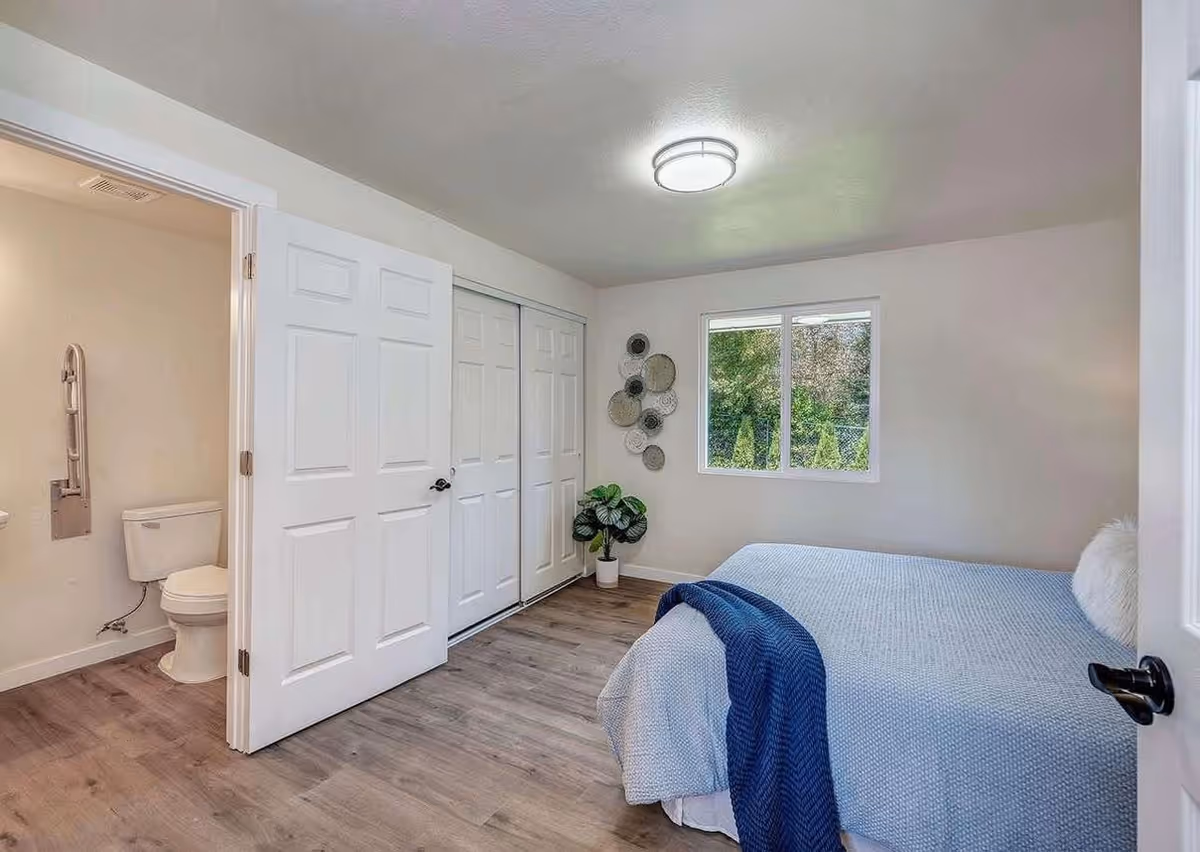 A tidy bedroom with a bed, closet doors, window, and an adjacent bathroom.