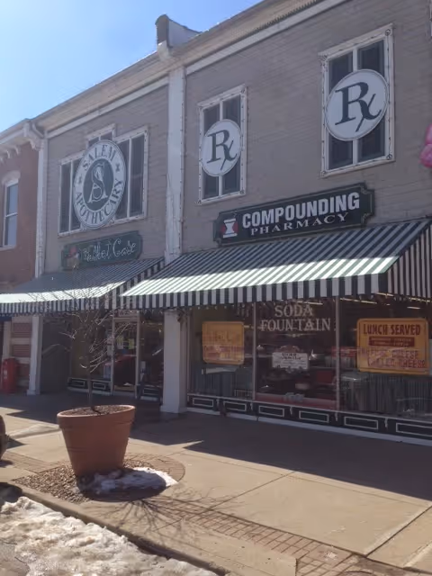 Exterior view of Salem Apothecary storefront with striped awning and pharmacy signs.