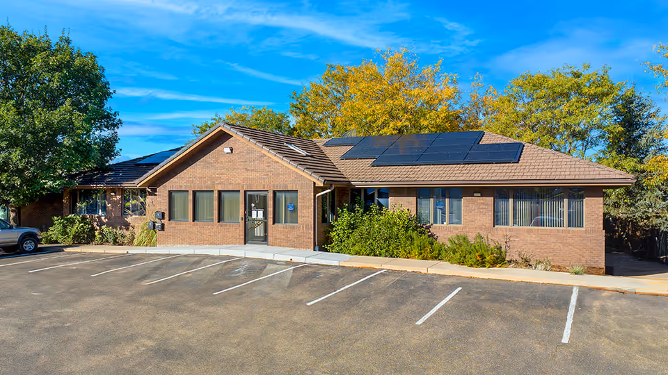 Single-story brick building with solar panels, a parking lot, and trees.