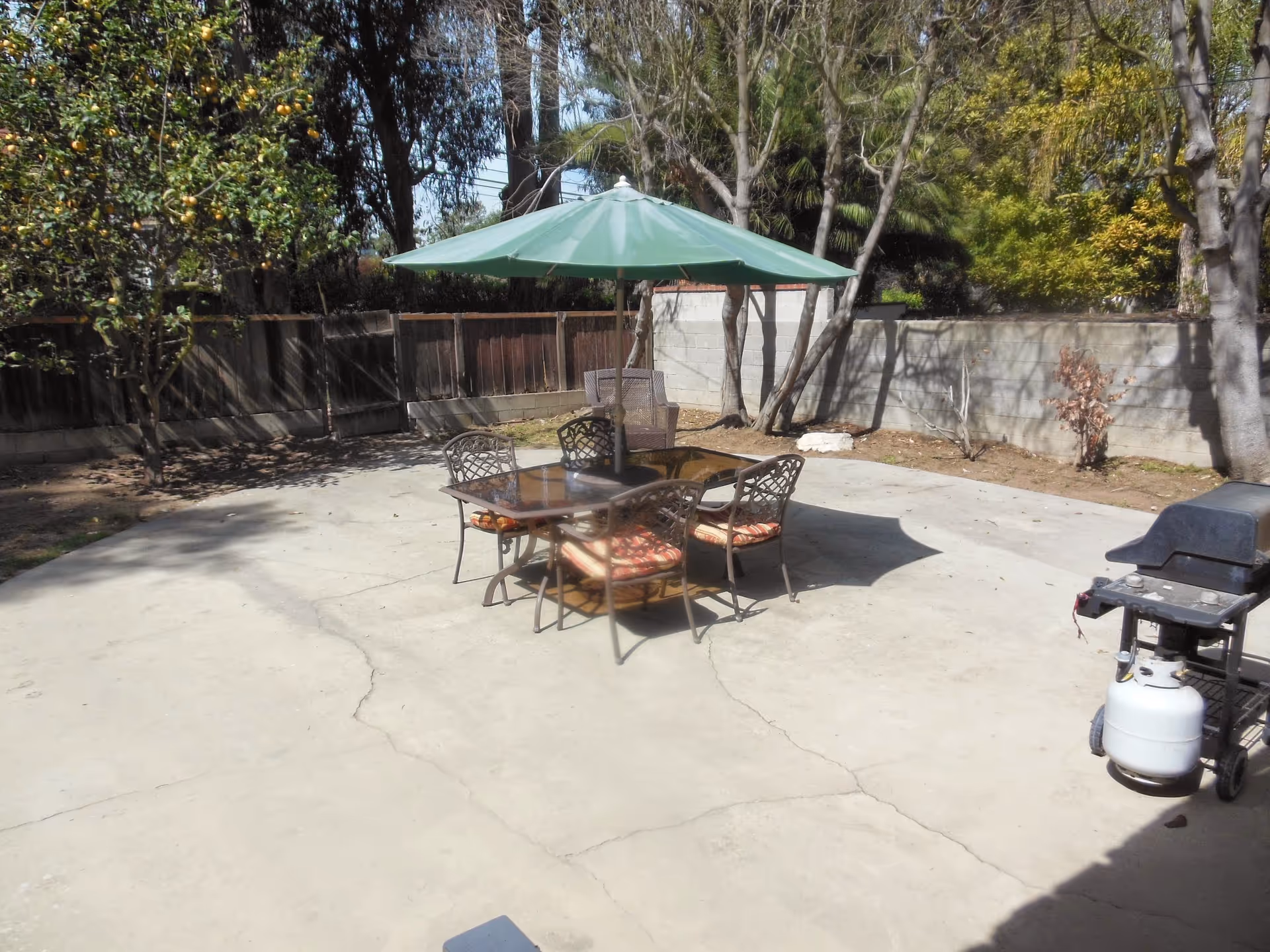 Outdoor patio with a table, chairs, umbrella, and a grill in sunny courtyard.