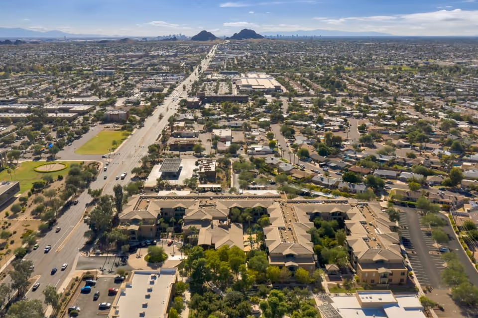 Aerial view of McDowell Village and surrounding neighborhood with a large road running through the area, numerous buildings, trees, and distant mountains under a clear sky.
