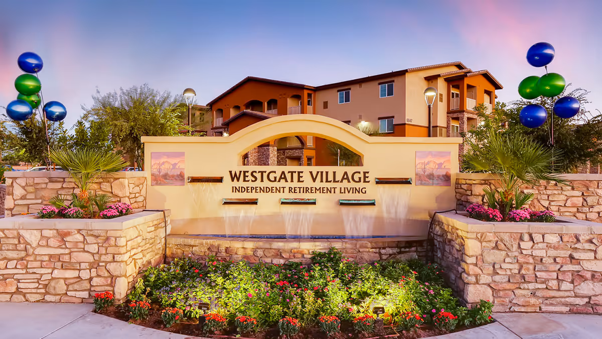Entrance sign and fountain reading 'Westgate Village Independent Retirement Living' with landscaped flowerbeds and the residence building in the background.