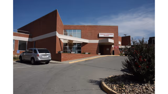 Brick hospital exterior with emergency department entrance, windows, and a parked car.