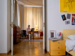 A person sits at a desk in a sunlit room viewed from a hallway.