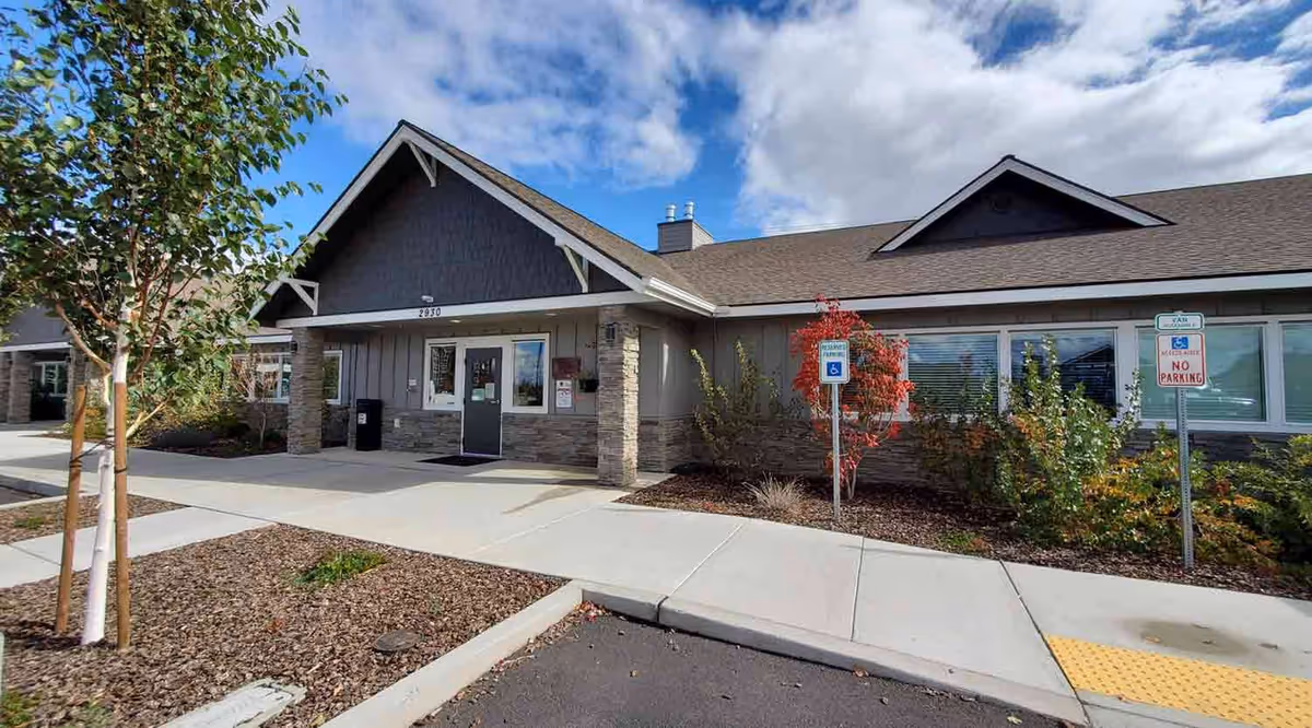 Front exterior of Juniper Canyon Living with entrance, landscaping, and a wheelchair parking sign.