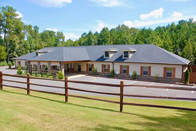 Single-story Premier Assisted Living building with manicured lawn, wooden fence, and parking lot.