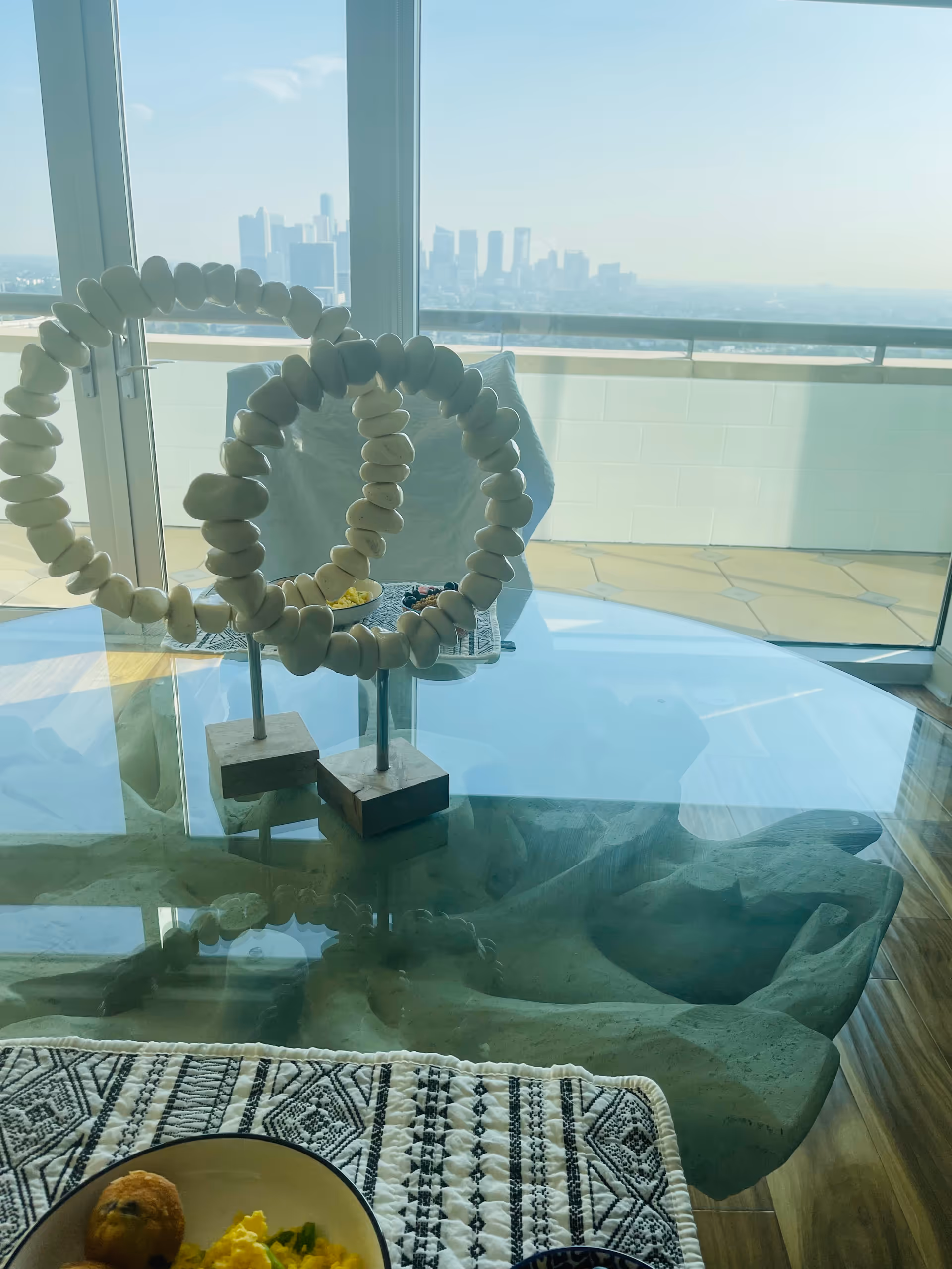 Decorative circular shell sculpture on a glass table with city skyline visible through a balcony window.