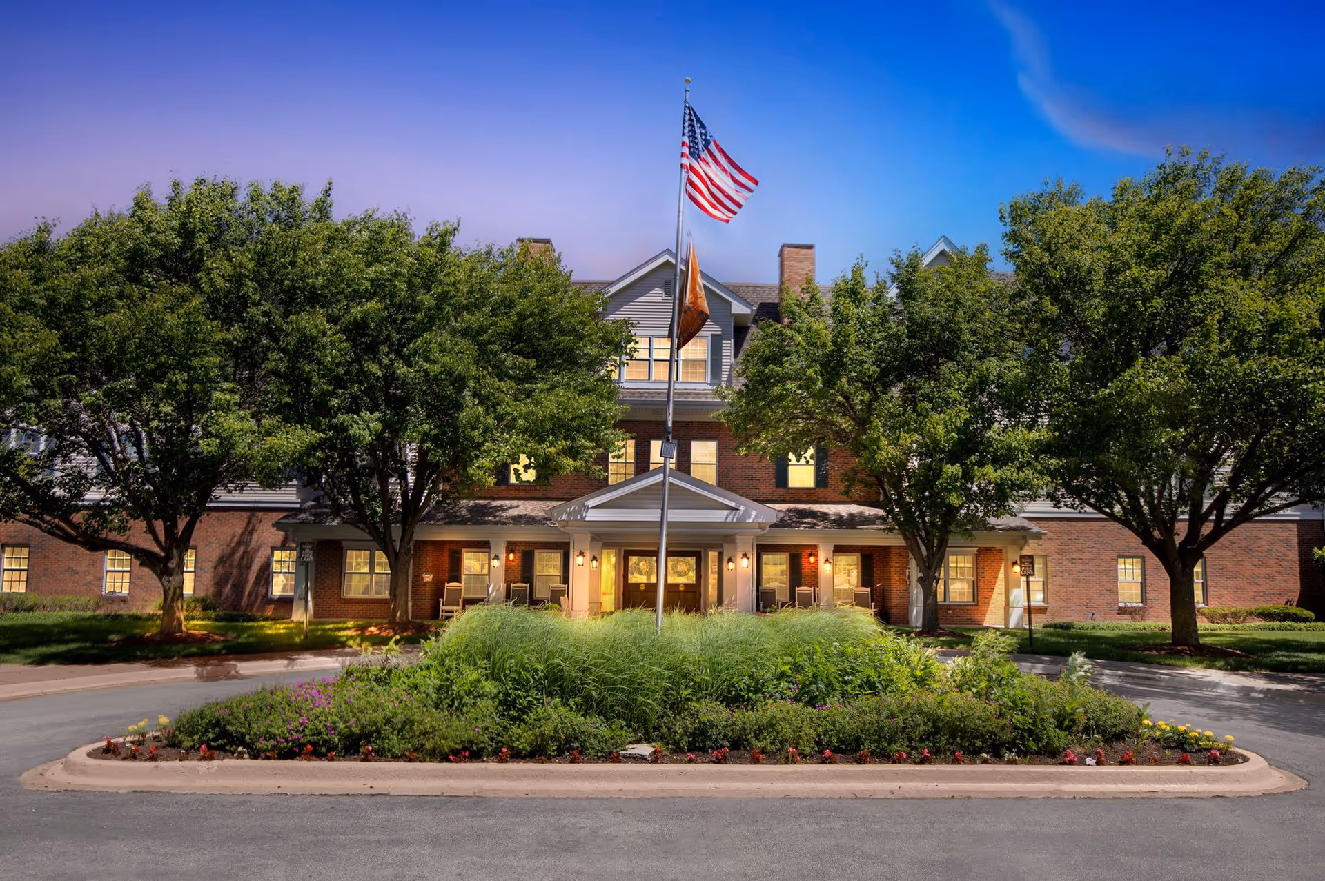 Brighton Gardens of Wheaton exterior featuring a flagpole, brick facade, and surrounding trees.
