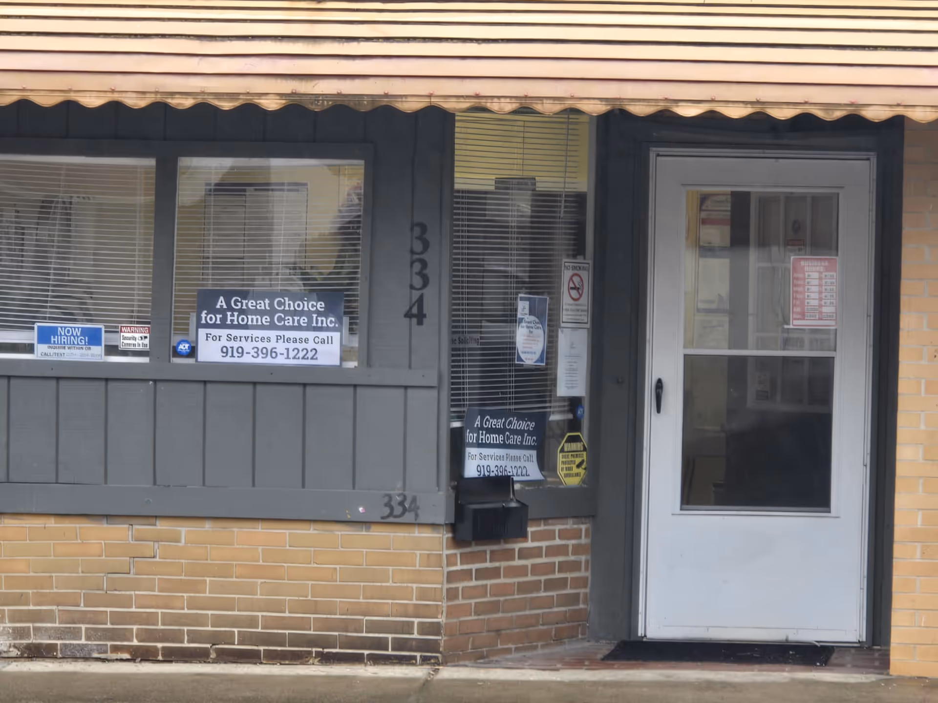 Front of a brick building with gray storefront and door with signs.
