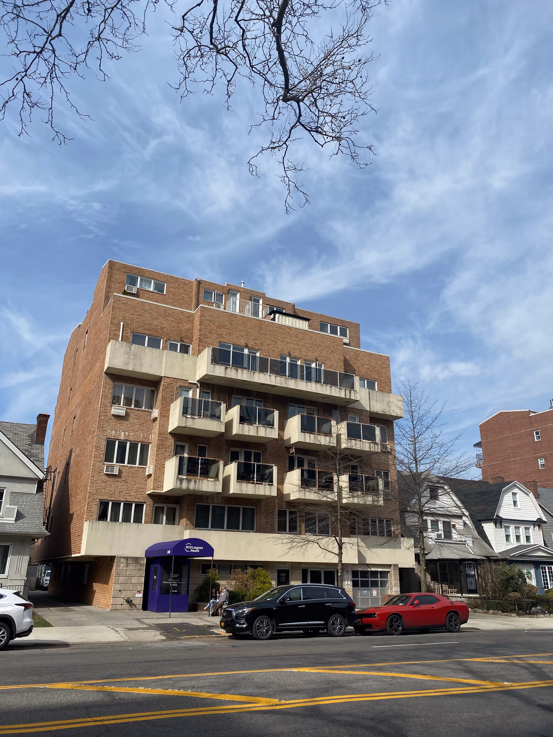 Brick mid-rise building with balconies and purple entrance awning on a city street