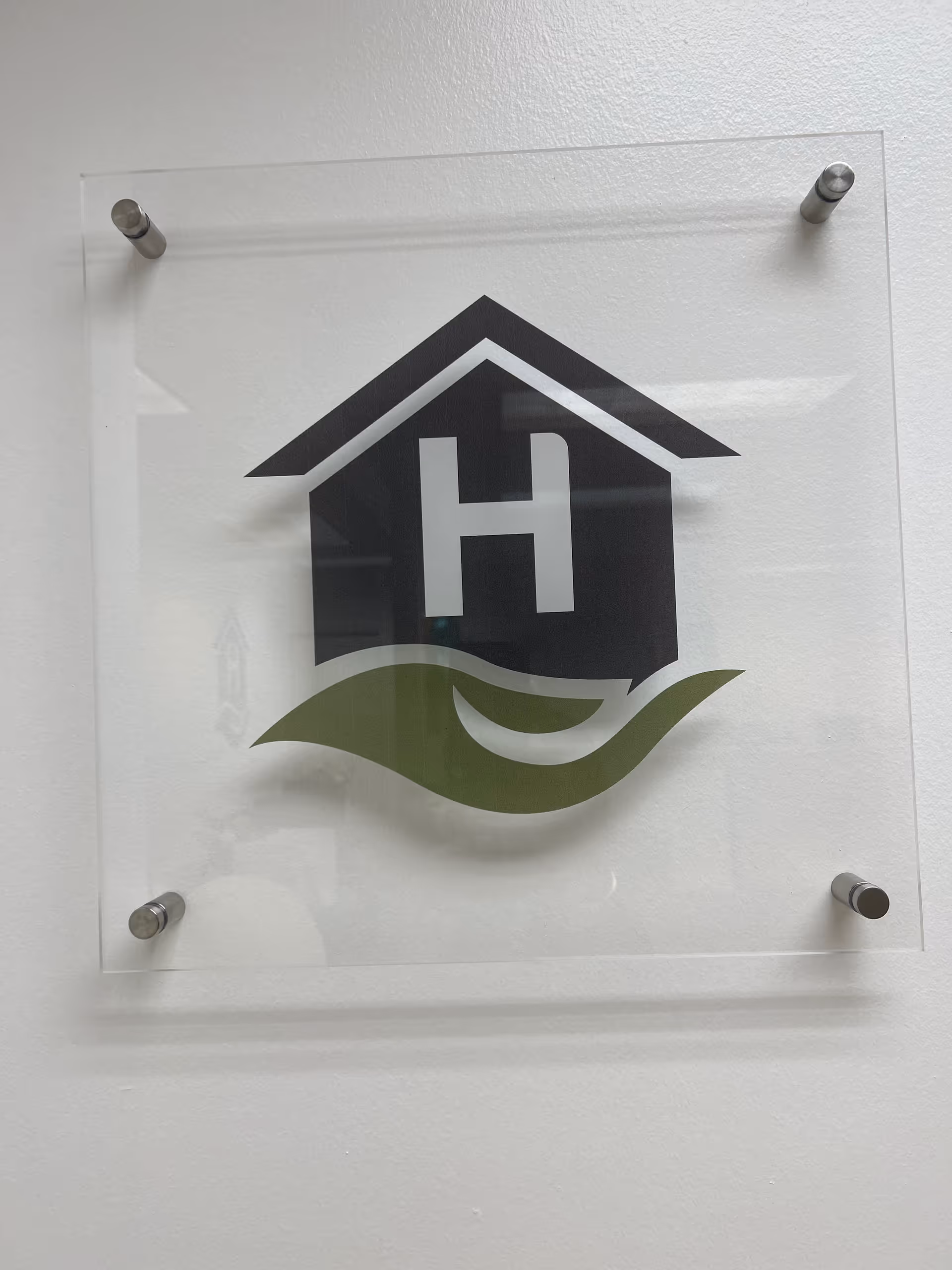 Clear sign with a black H inside a house shape and green curved accent on wall.