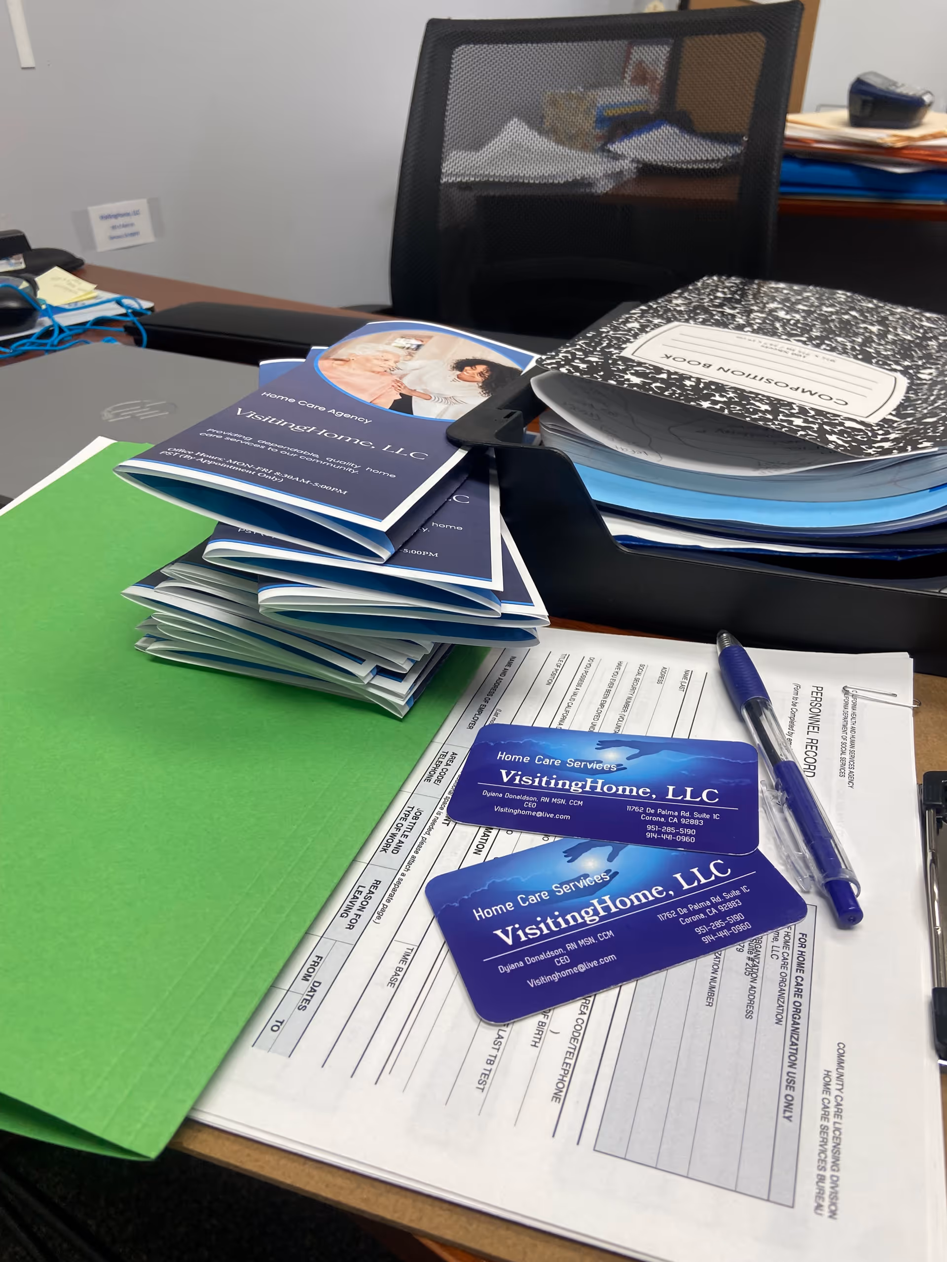 Office desk clutter with VisitingHome LLC business cards and folders.