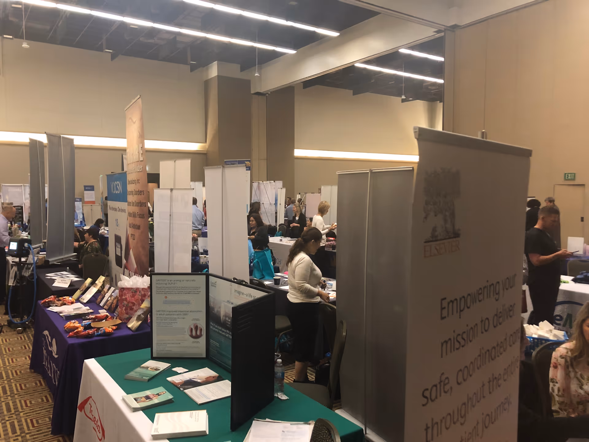 Indoor exhibition hall with multiple vendor booths and attendees at a senior care expo
