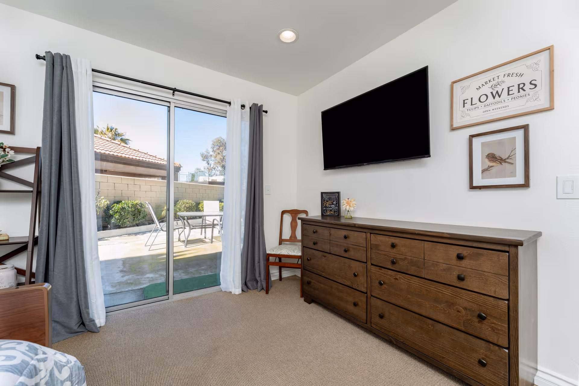 Senior living bedroom with dresser, wall TV, chair, and sliding glass door to patio.