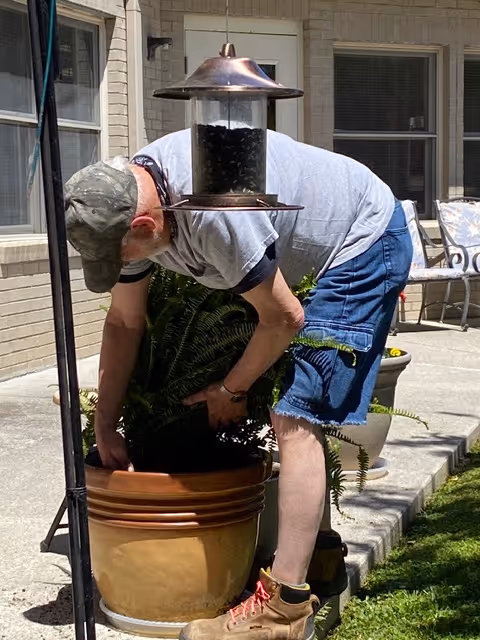 Person plants in a large pot on an outdoor patio beside a house.