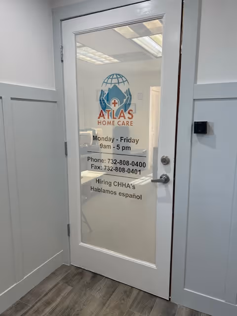 Glass door with Atlas Home Care logo and business hours in a light hallway.
