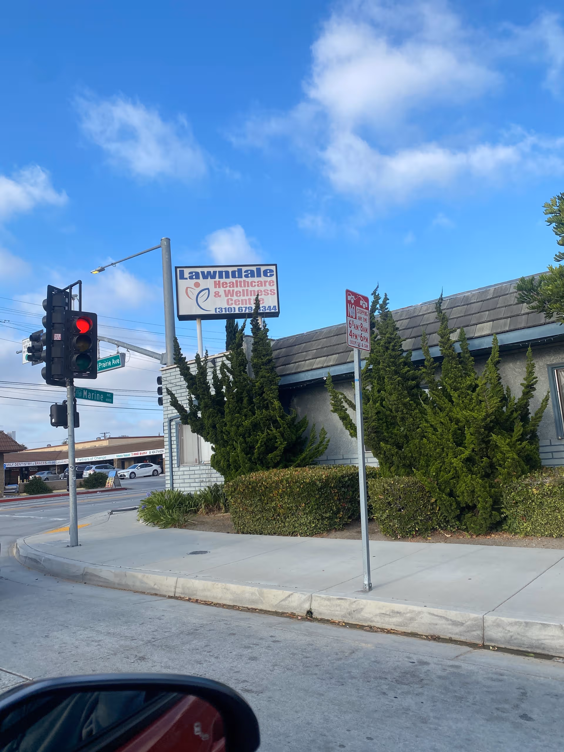 Street view of a building exterior with a sign and trimmed shrubs beside sidewalk
