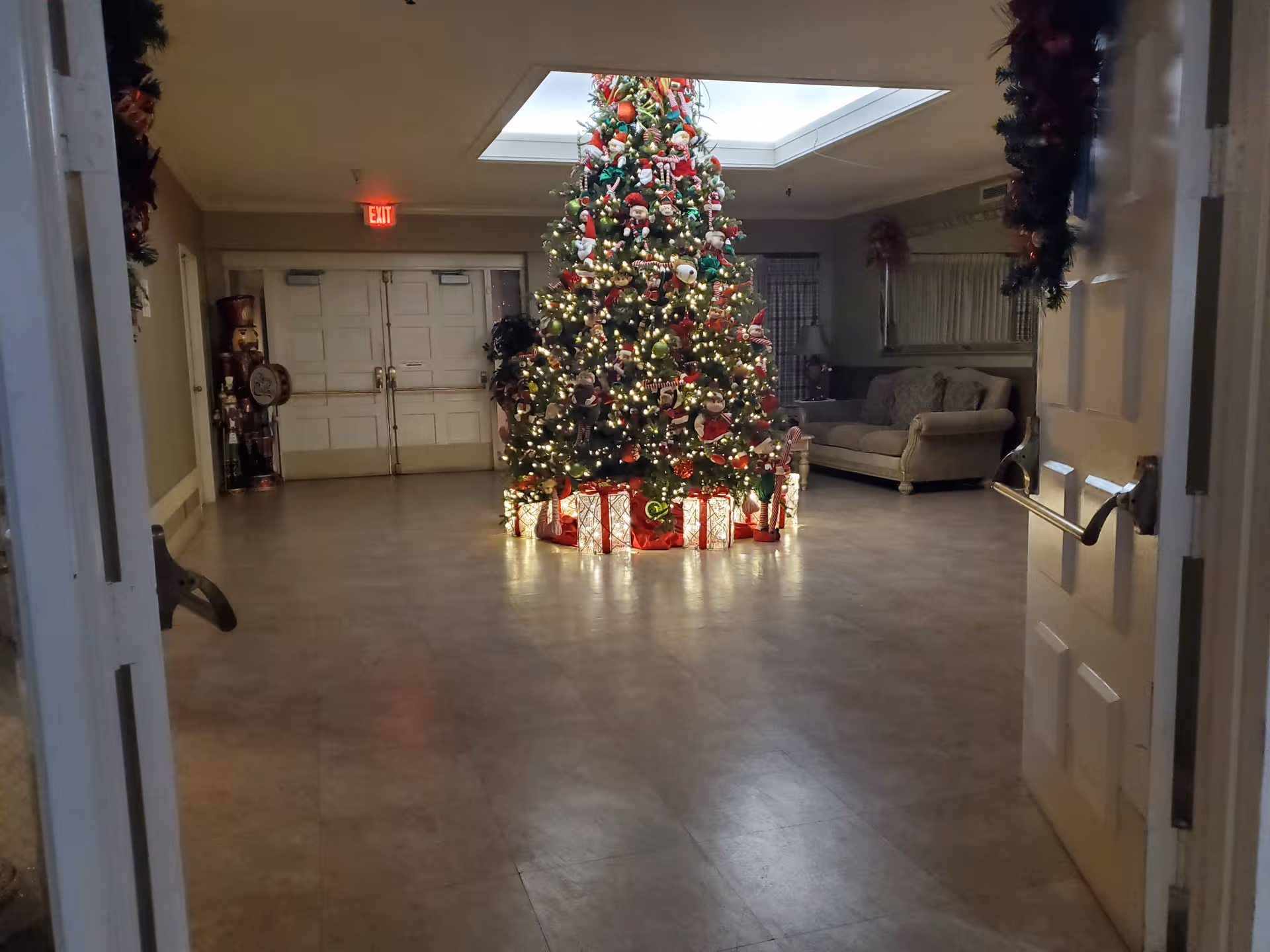 A tall, decorated Christmas tree stands in a hospital lobby beside a couch and double doors.