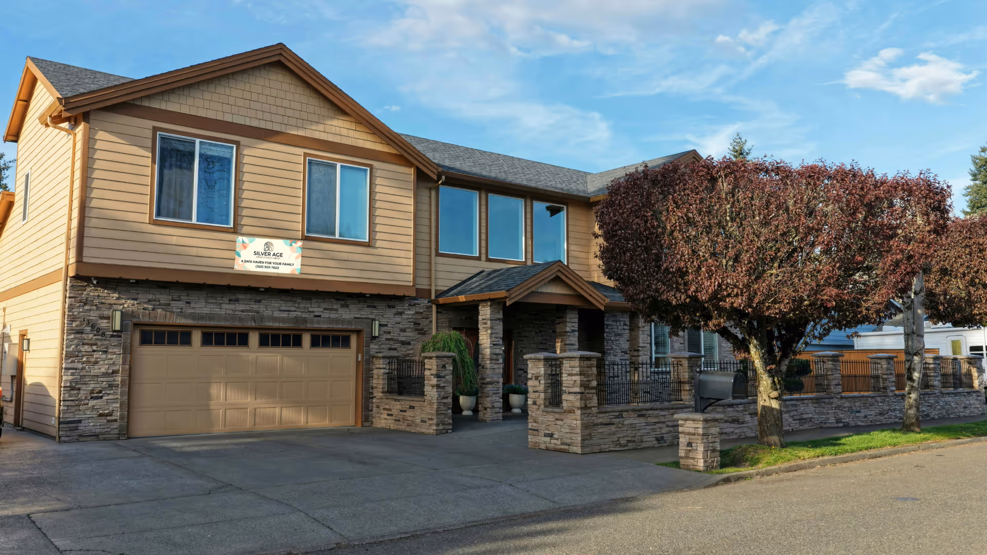 Two-story beige senior living building with stone accents and a landscaped front yard.