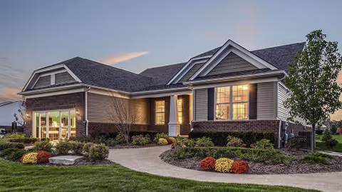 Single-story senior living facility with a lit front entrance, curved walkway, and landscaped shrubs.