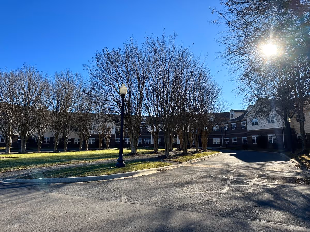 Sunlit exterior view of a two-story senior living building with leafless trees and a circular driveway.