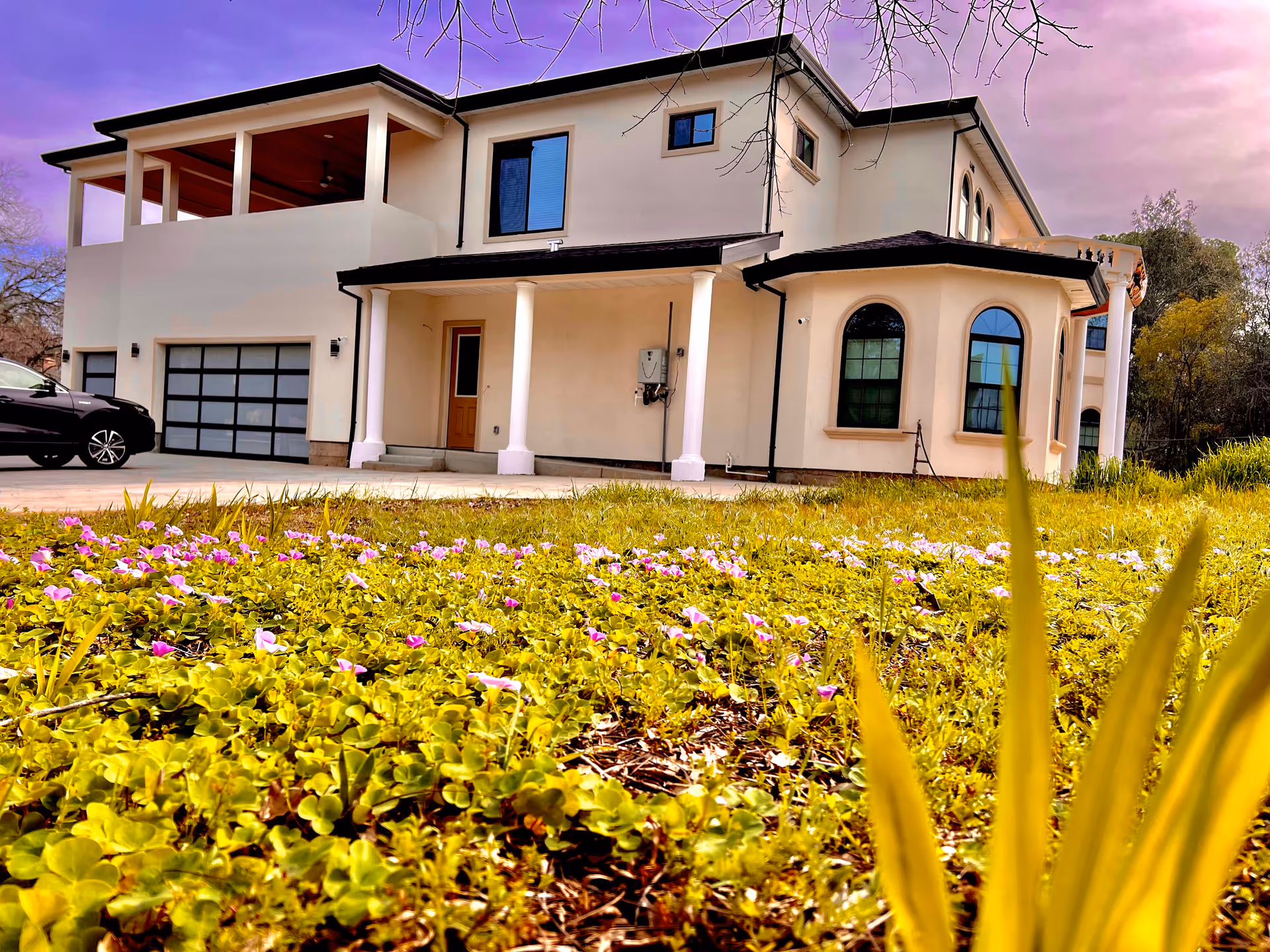 Modern two-story care facility exterior with columns, garage, and blooming front yard.