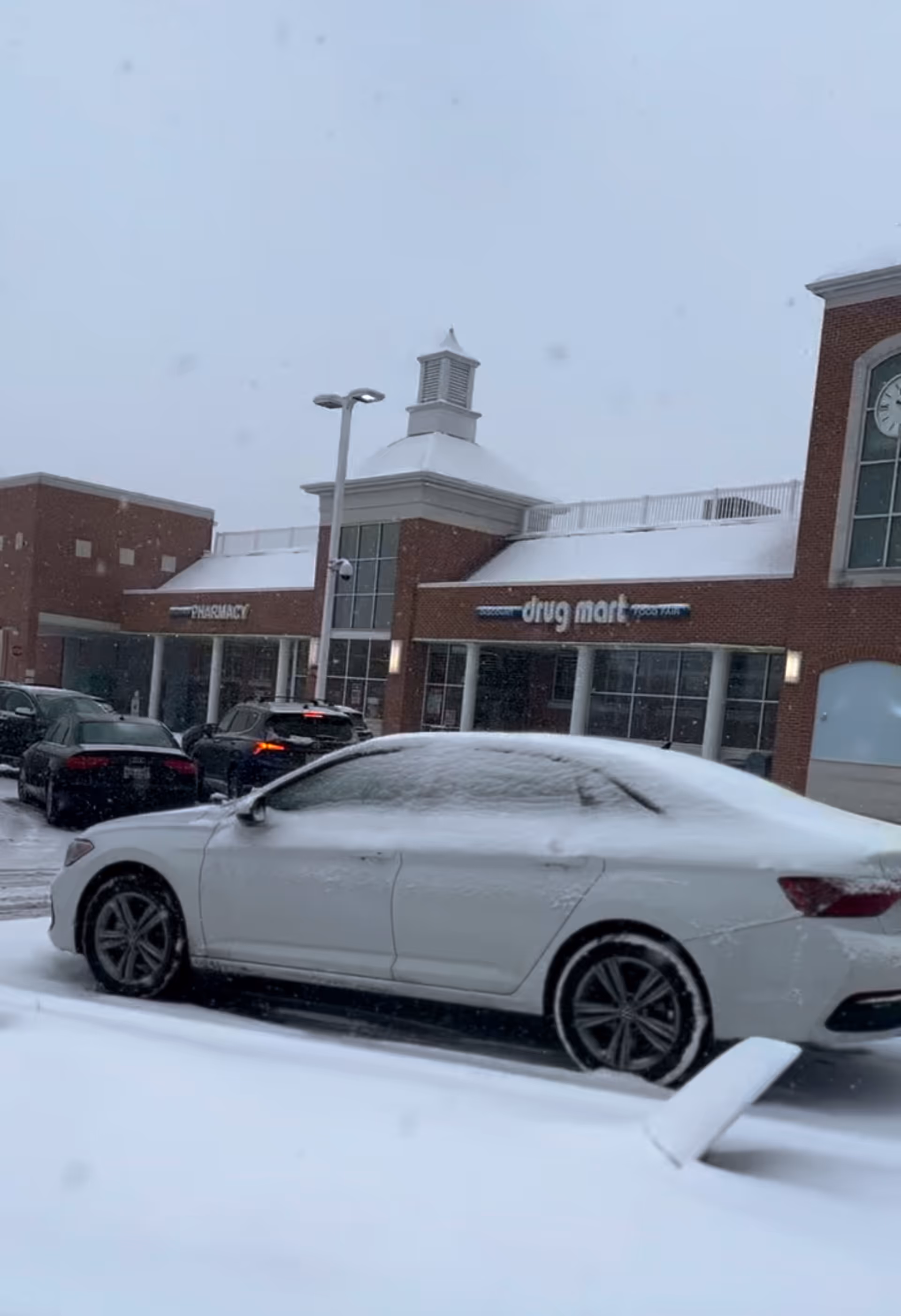 Snow-covered Discount Drug Mart storefront with parked cars in a snowy lot.