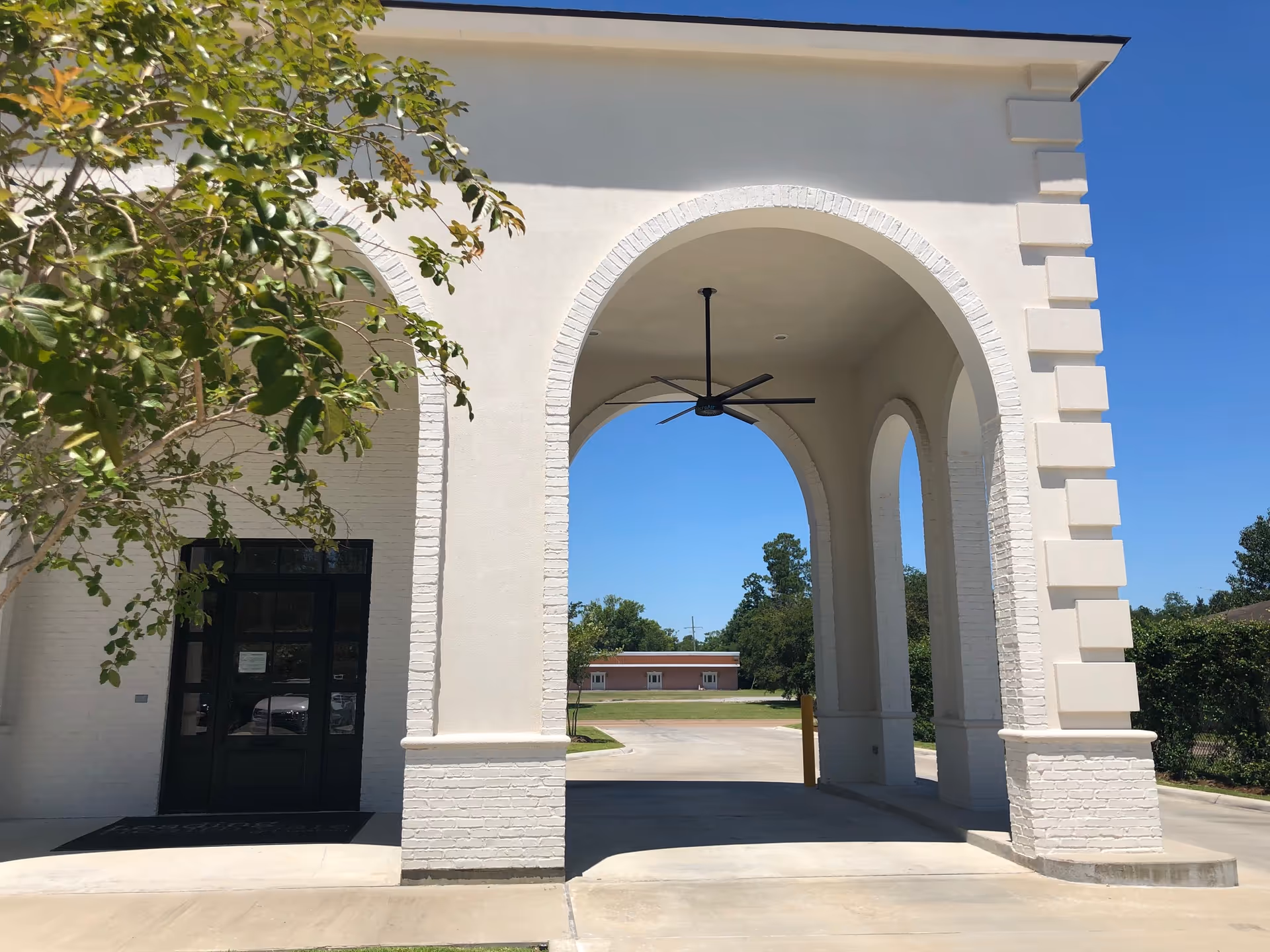 Exterior view of a white brick arched entrance with a ceiling fan.
